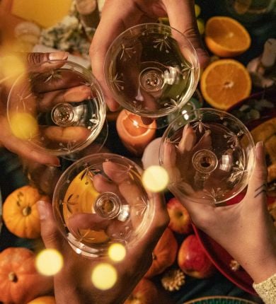 image of a table of thanksgiving food and people clinking cocktail glasses together in the center
