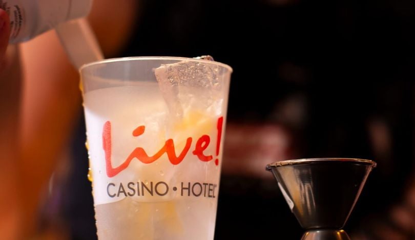 image of a white cup with ice that says Live! Casino and Hotel and a woman pouring drink syrup into it