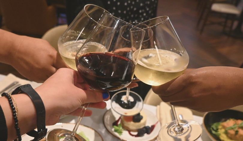 image of 4 wine glasses clinking together over a table of italian food on a white table cloth