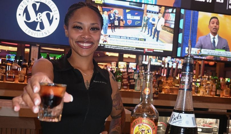 image of girl with sports & social louisiana top on holding a shot glass with black and gold liquor
