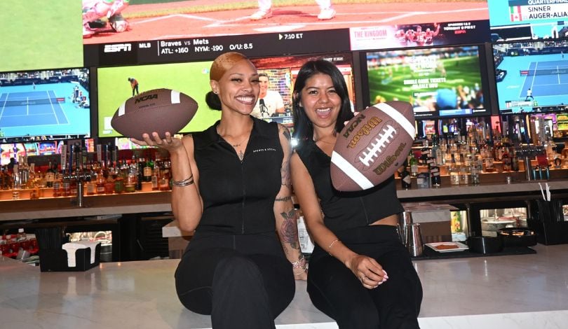 image of two girls sitting on a bar top holding footballs