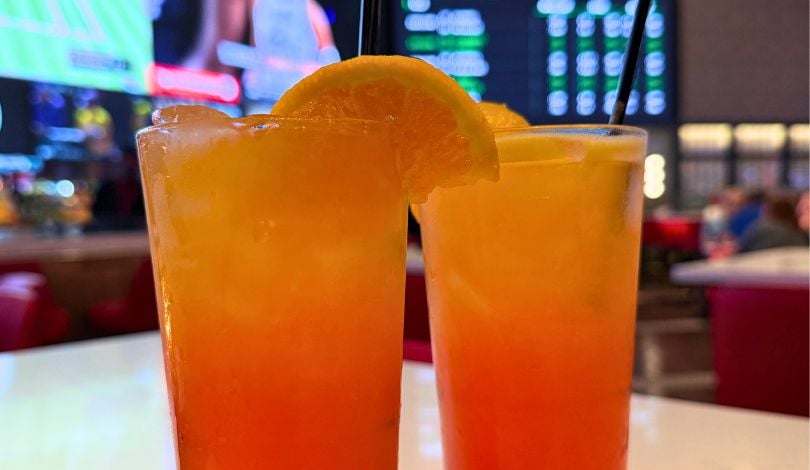 image of two glasses with tequila sunrise cocktails in tall glasses with oranges on top