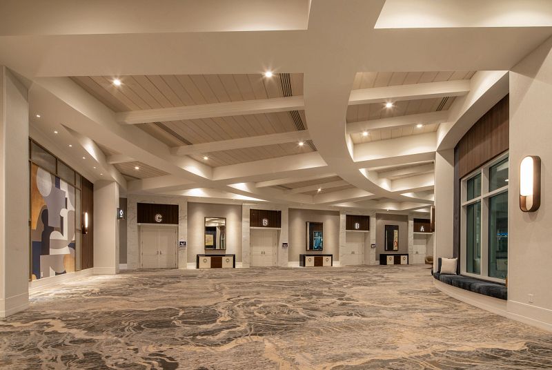 Large open space with grey and white carpets, doors with the letters A, B, and C are on the far side of the room leading into the Event Center.