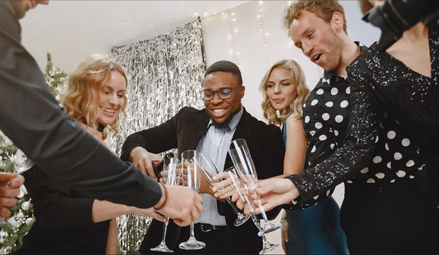 Four people in semi formal attire pouring champagne while looking excited