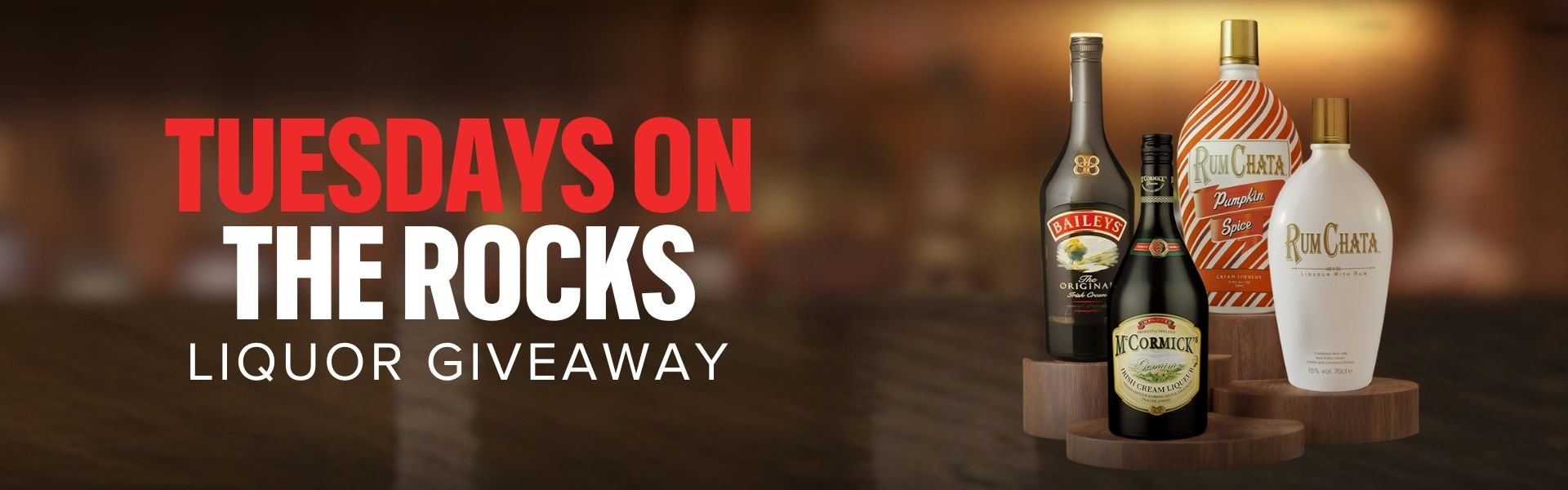November Tuesdays on the Rocks. 4 different types of liquor sitting on wooden stands with a blurry bar background.