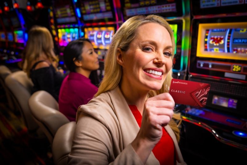 Woman at a slot machine holding a Live! Rewards Classic Card