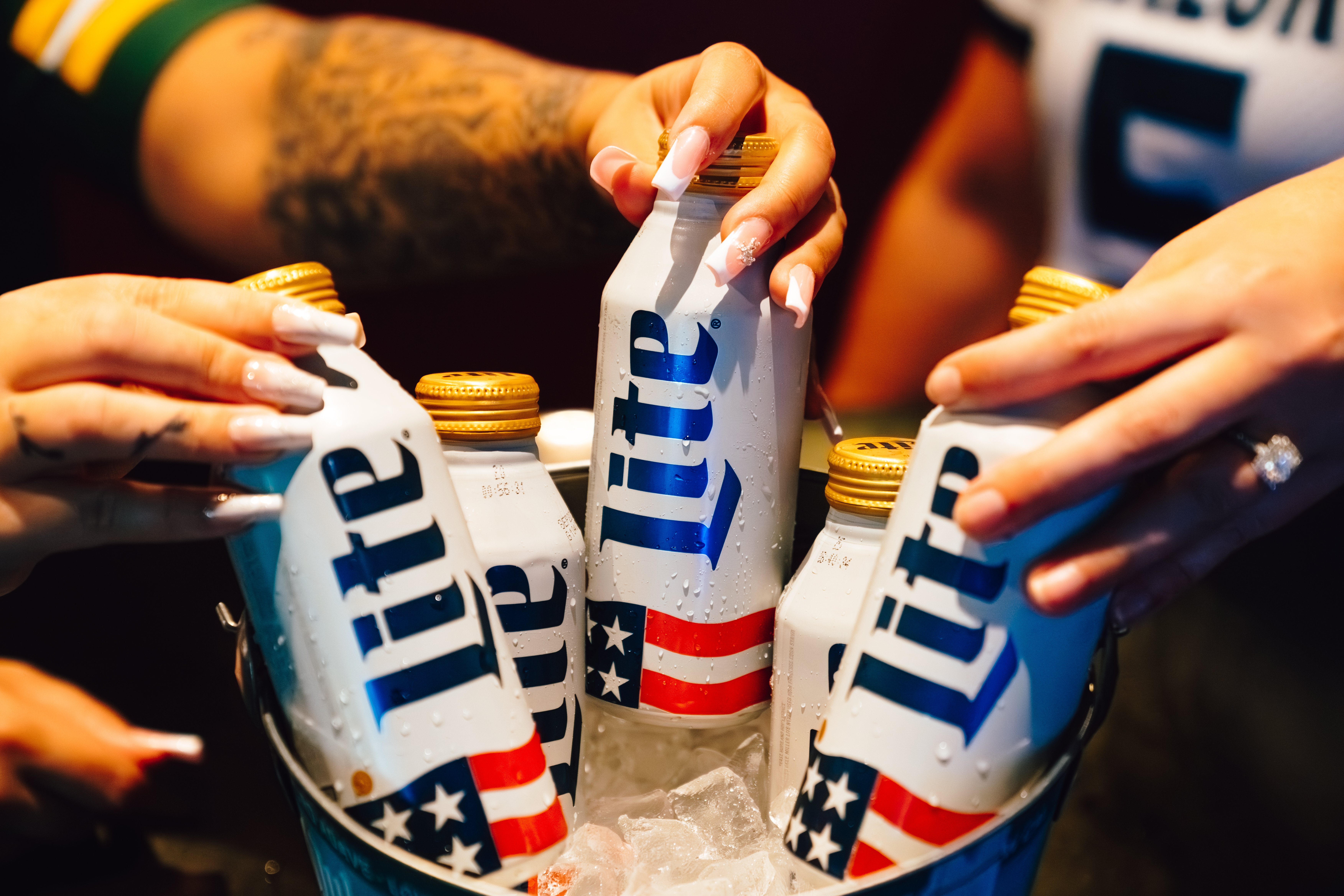 An image of people's hands reaching for beers in a bucket.