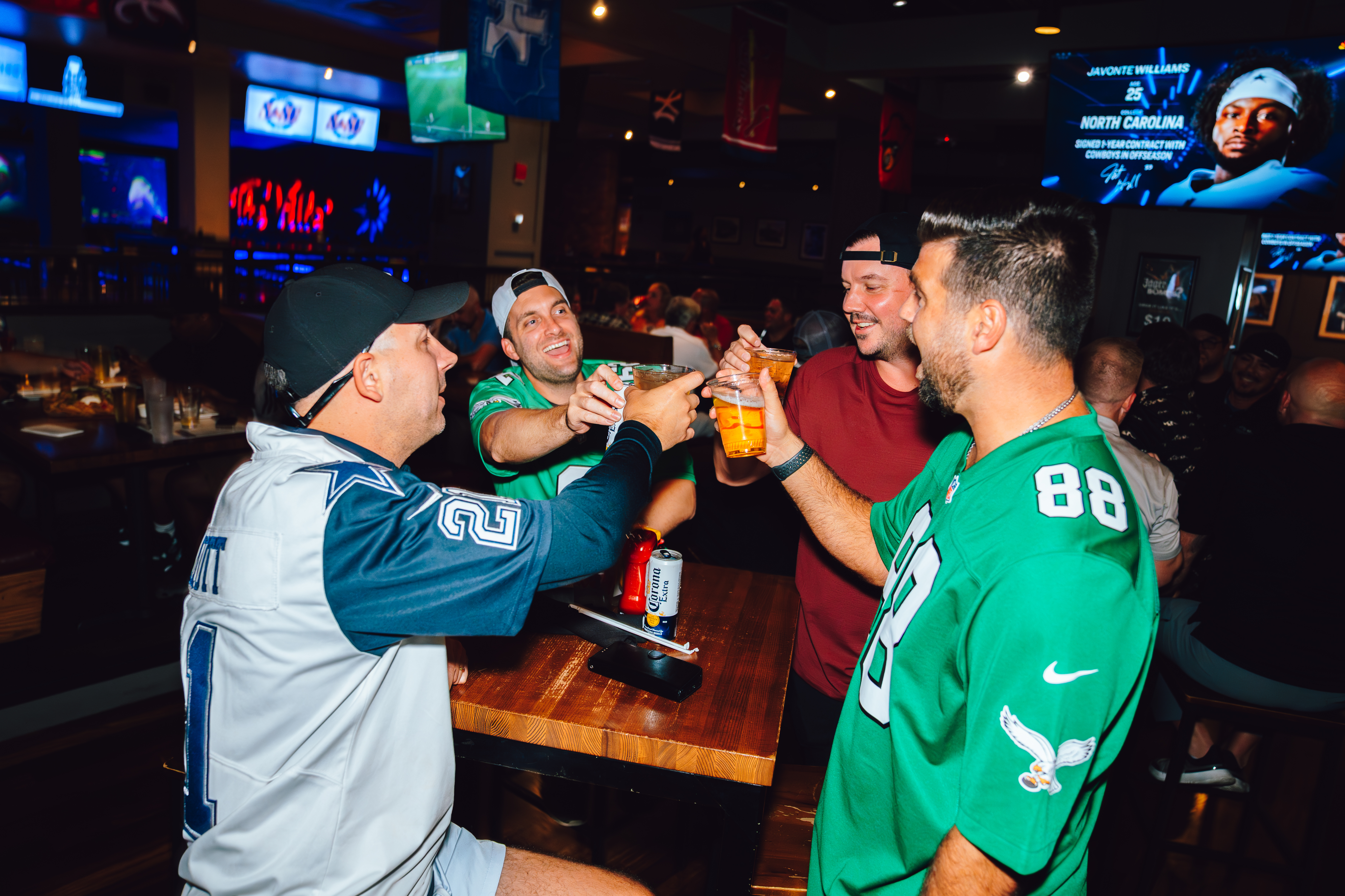 An image of people in football jerseys cheersing beers.