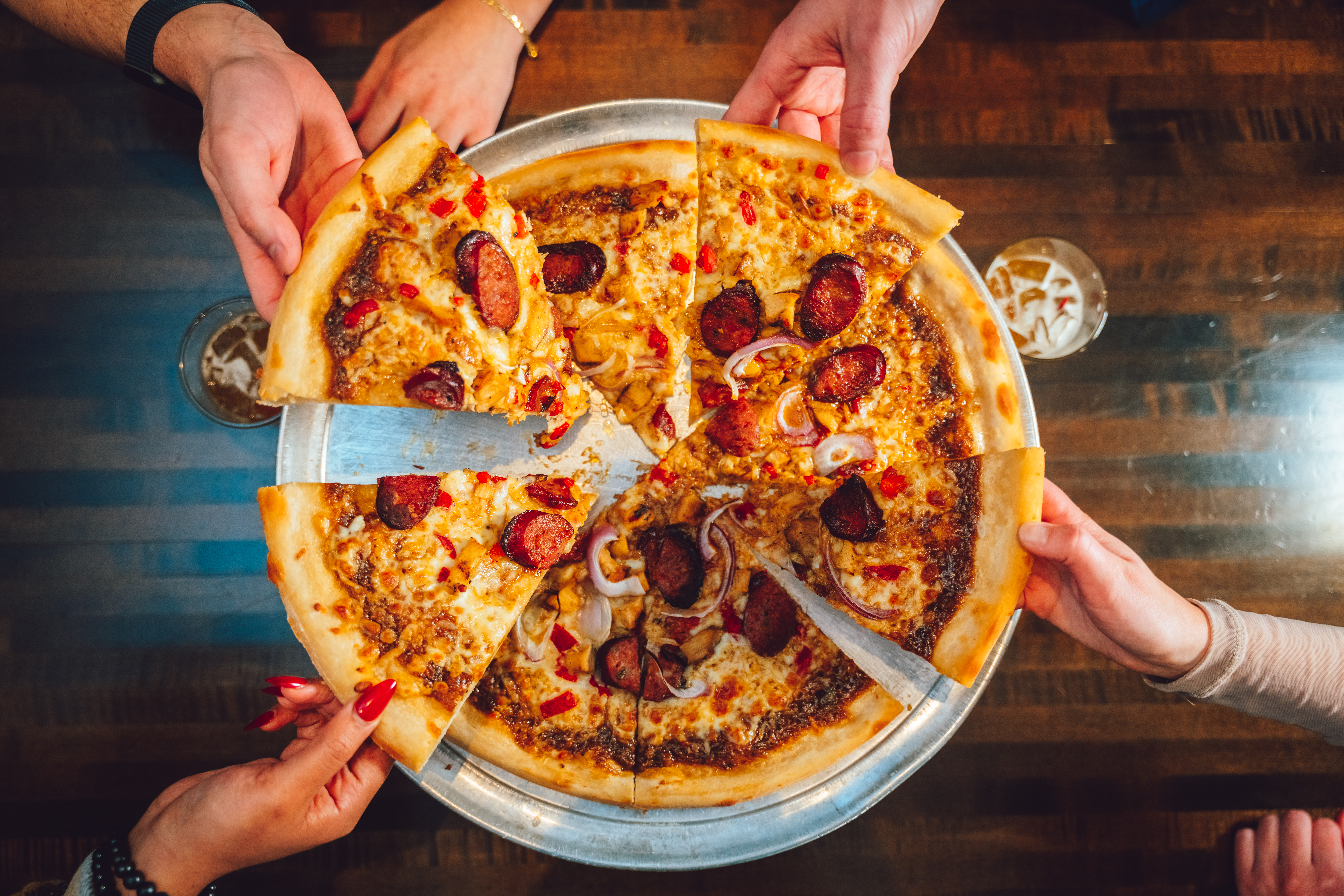 Group grabbing pizza slices from a whole pizza.