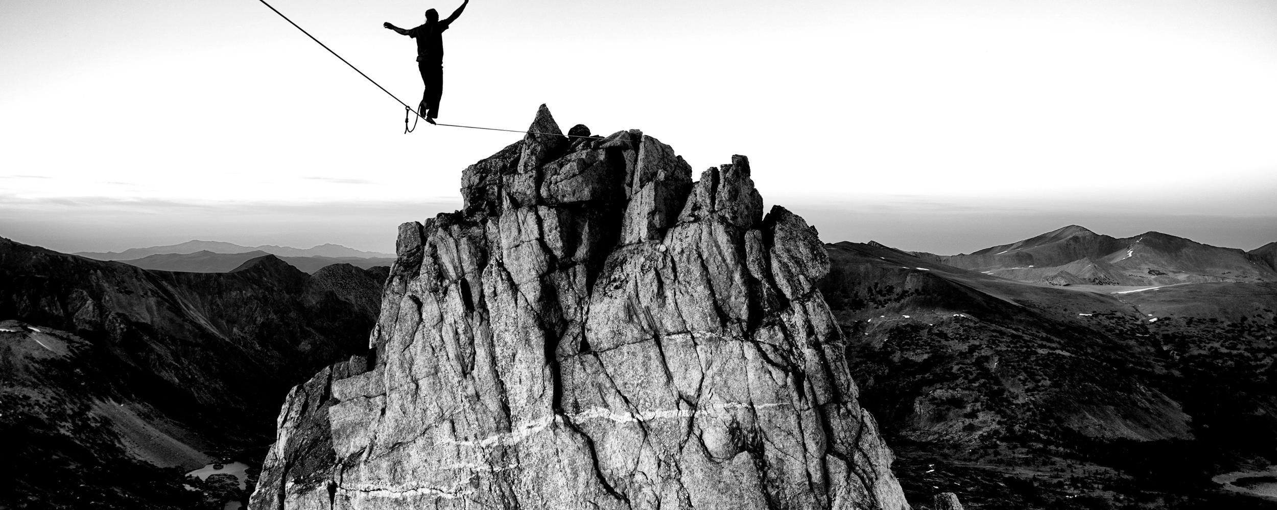 A person on a tightrope walking towards a large mountain