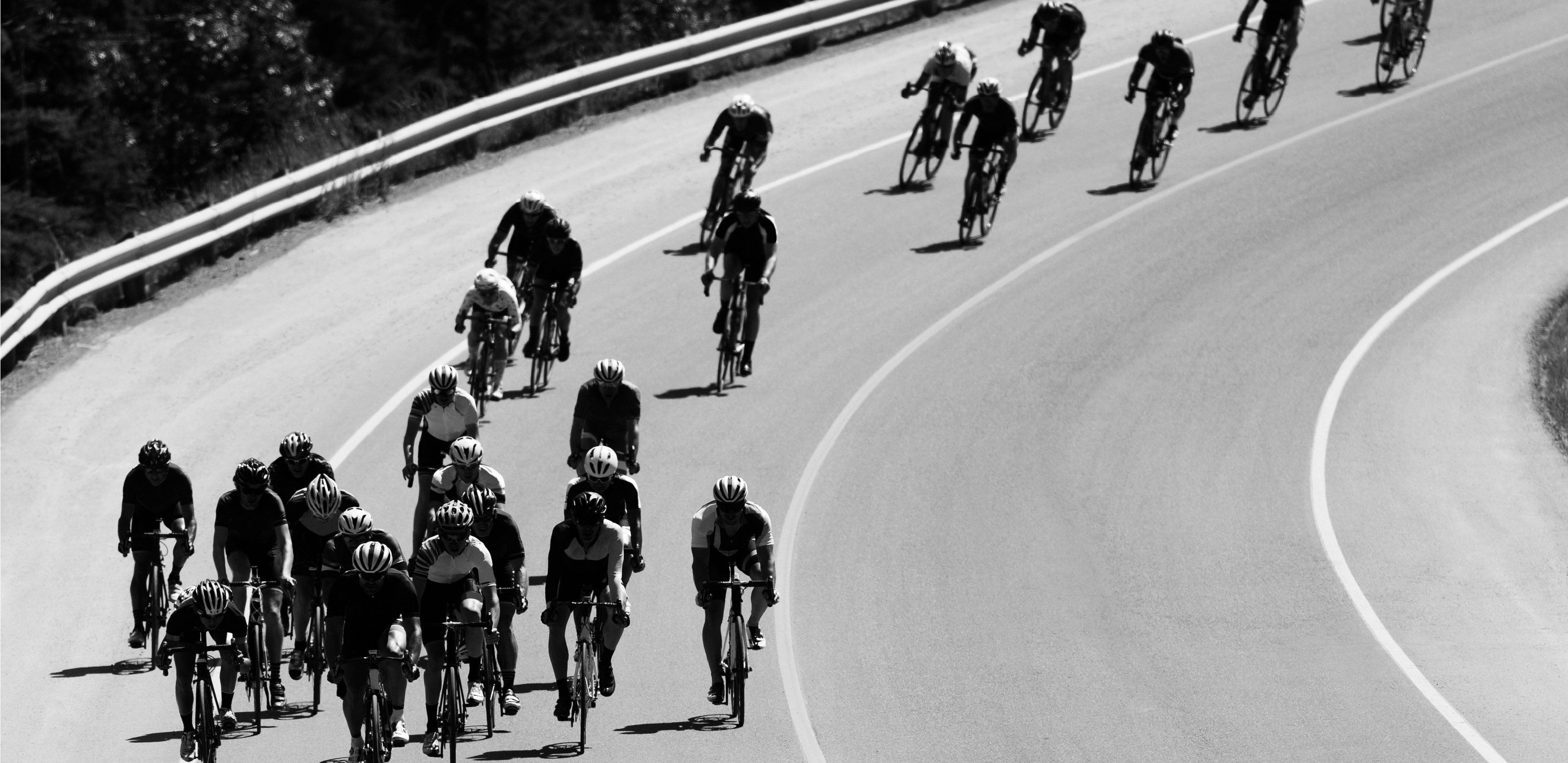 A group of men ride together during a road bicycle race on a sunny day.