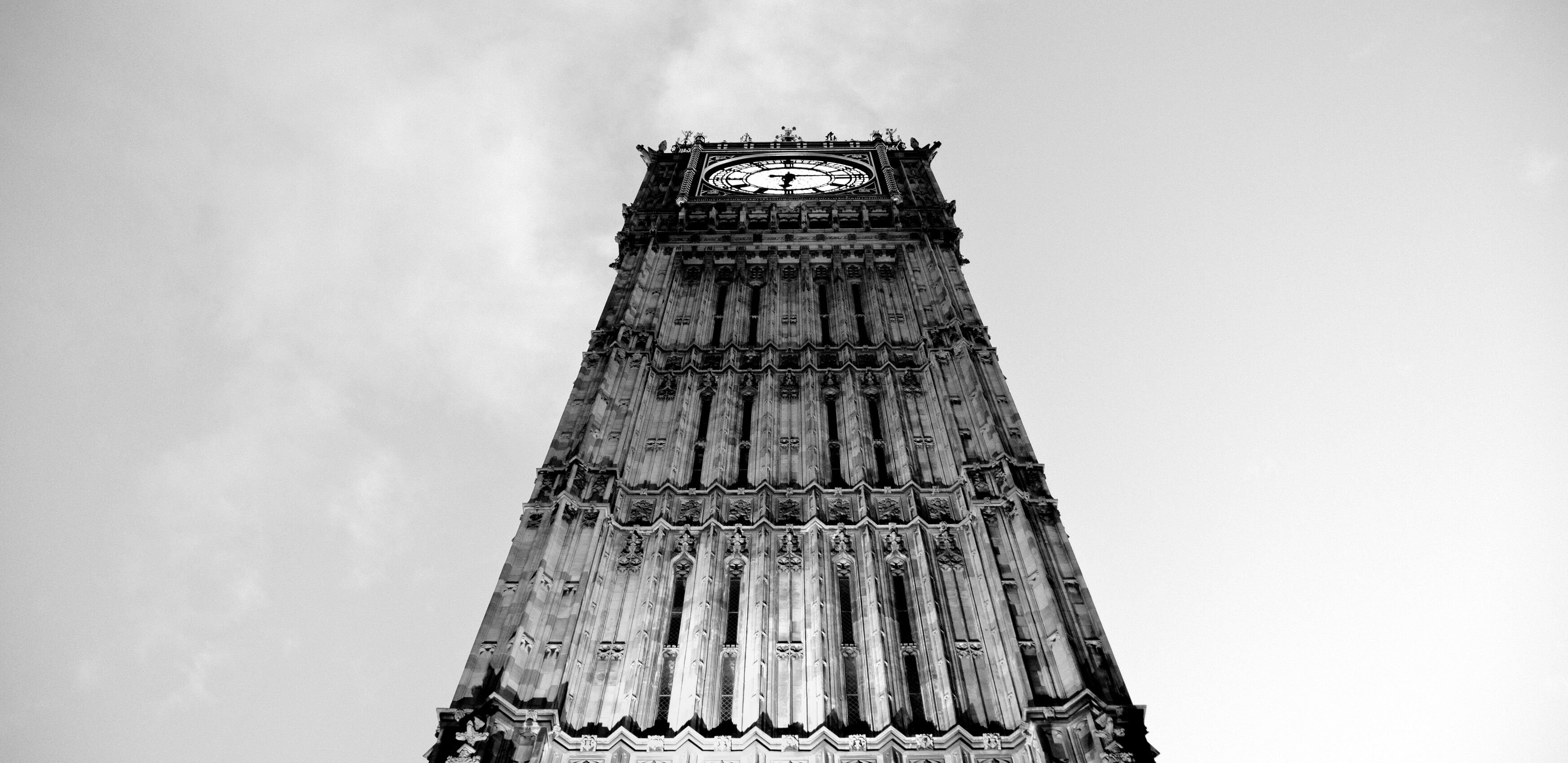 A large clock tower, from below, with grey clouds surrounding it