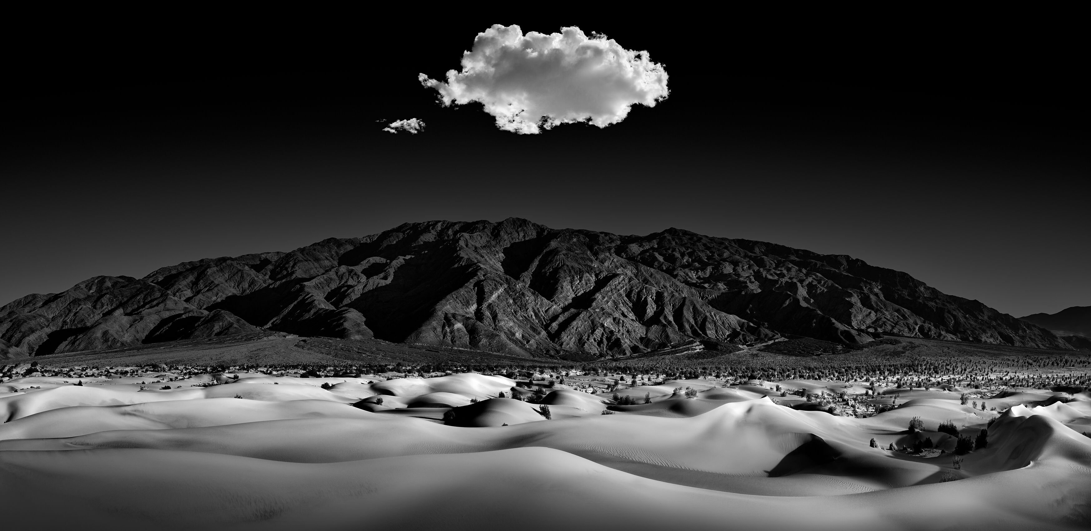 A cloud hovering over a desert with mountains in the distance