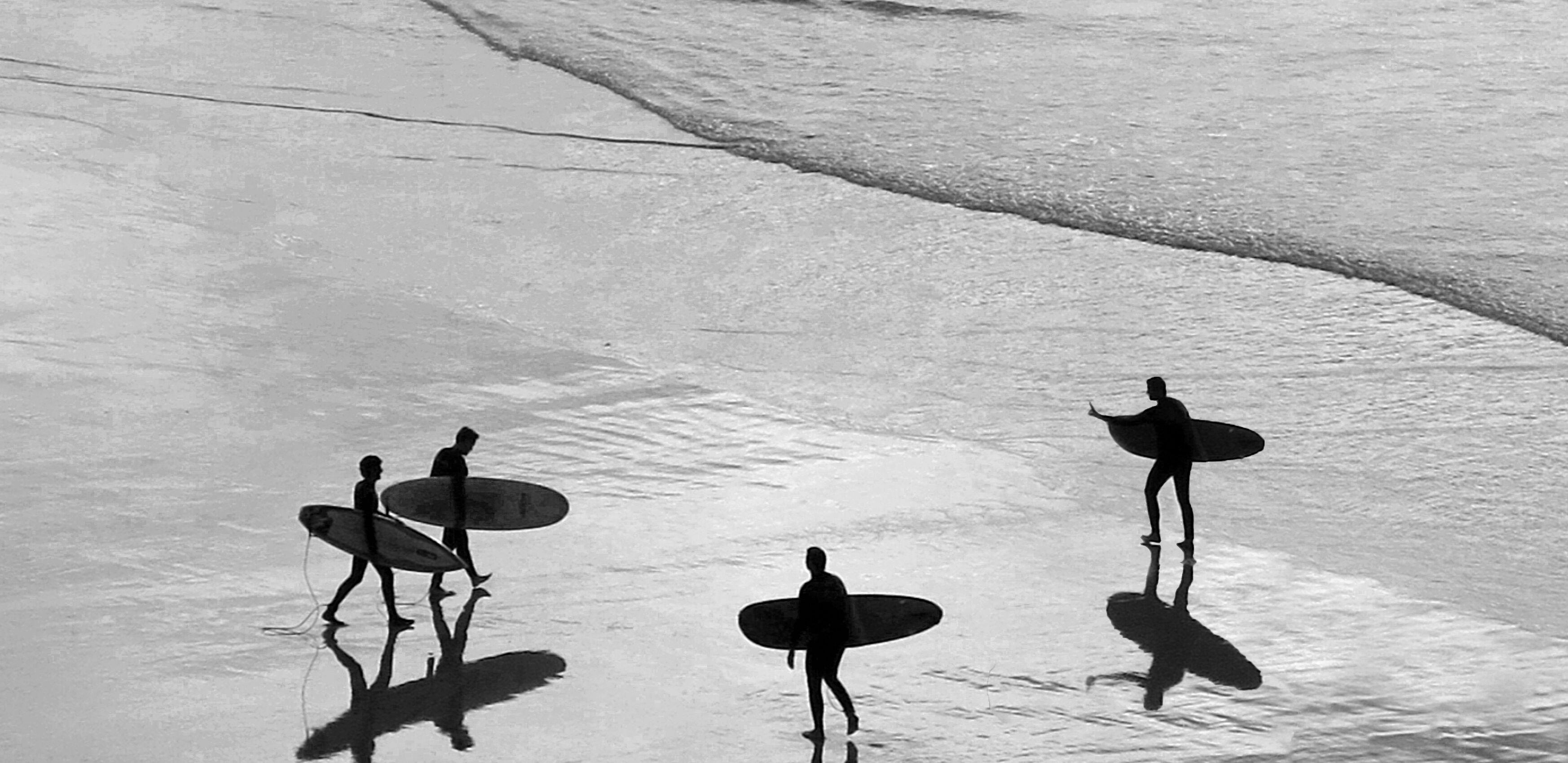 Five surfers walking into the water with their shadows being cast onto the beach