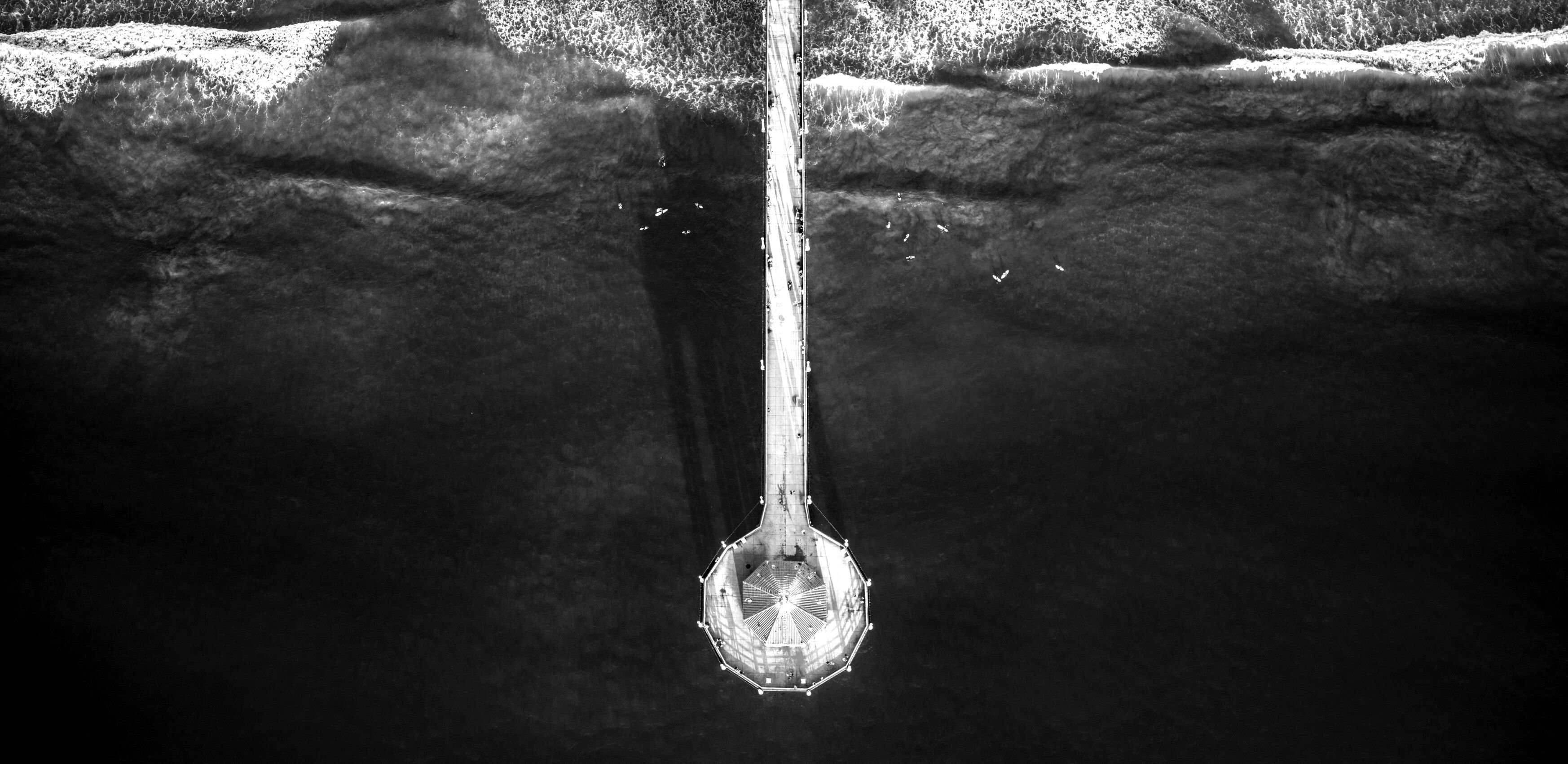 A pier going out to sea, with multiple surfers in the water