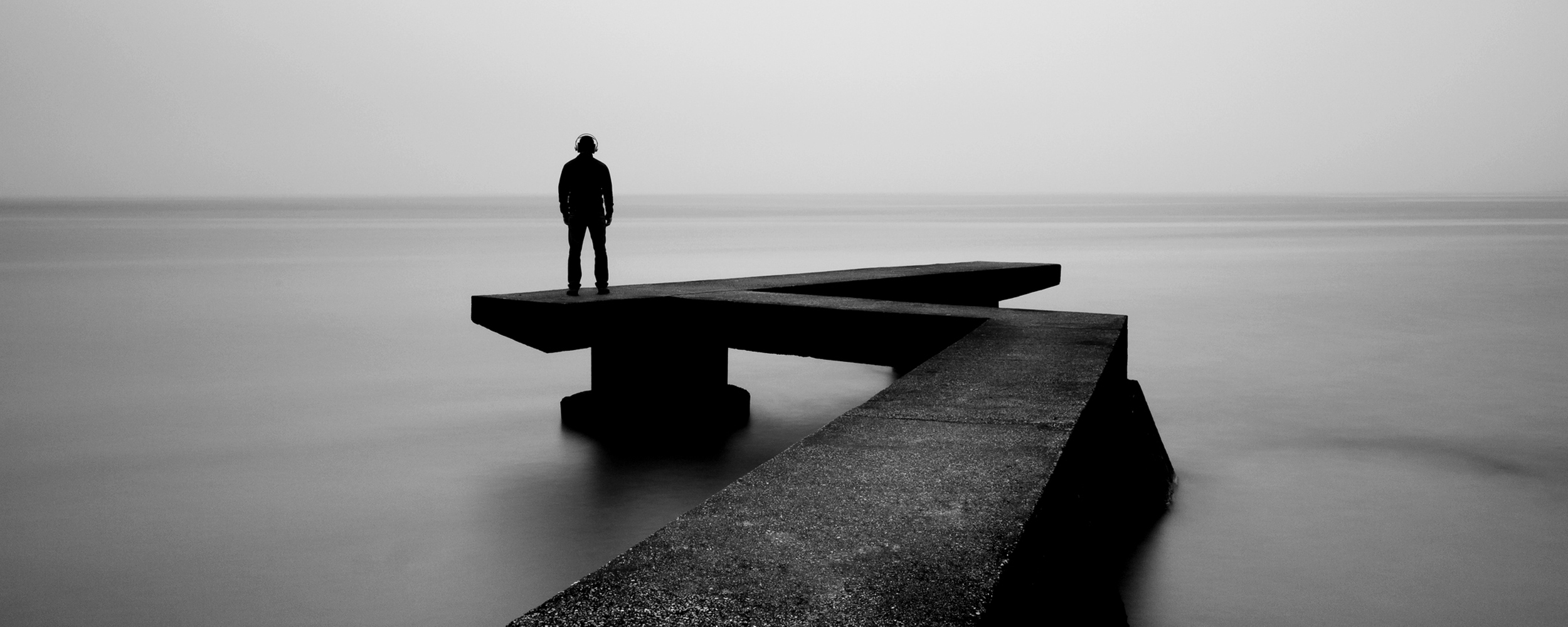 One person looking at the horizon, looking at the sky, black and white image, pier over Rio de La Plata..Man with headphones..Image taken outdoors