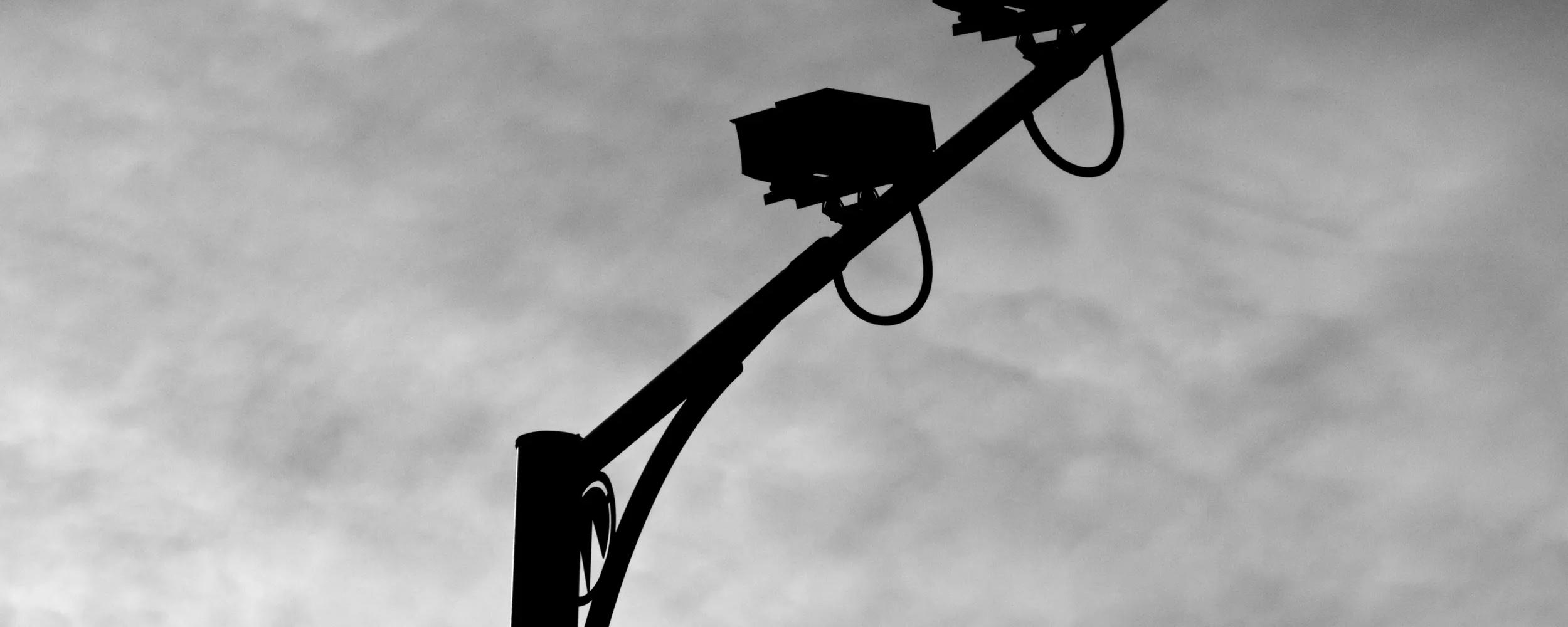 Multiple speed cameras monitoring traffic on UK motorway. Cameras are silhouetted against a cloudy background.