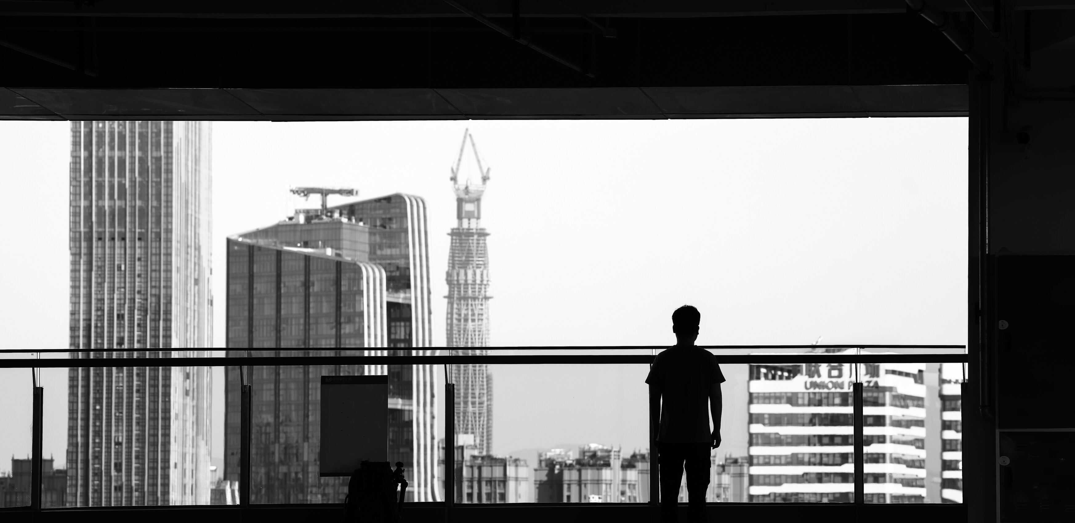 A person standing on a balcony, looking onto a modern city with large skyscraper buildings
