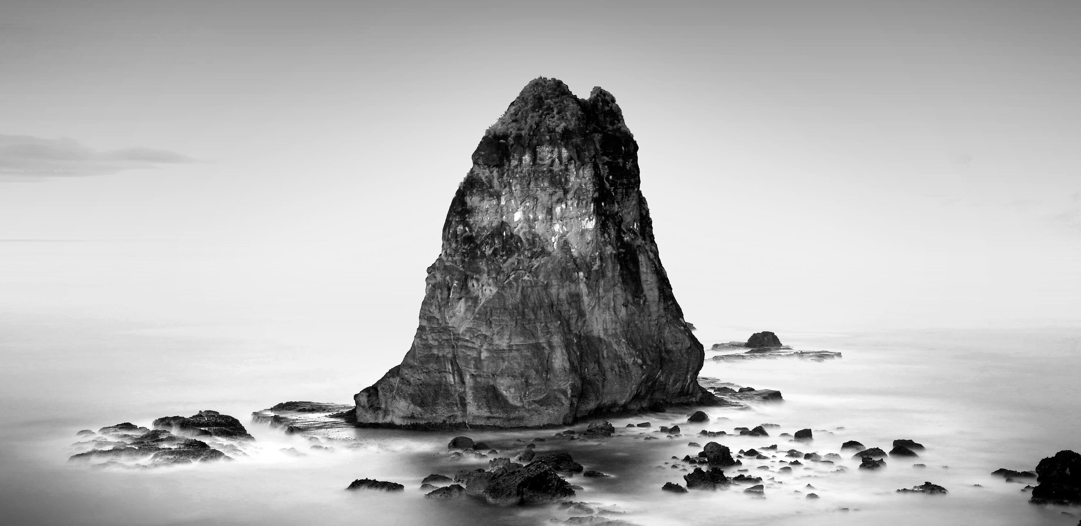 A large rock, showing through the ocean with low hanging fog