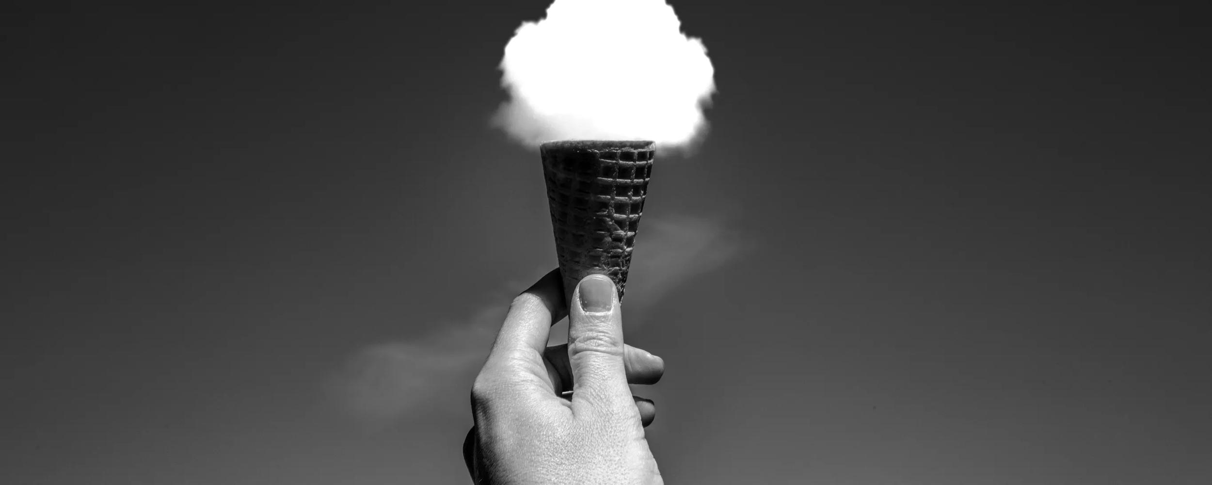 A hand holding a cone in front of a cloud to give the illusion of ice cream.