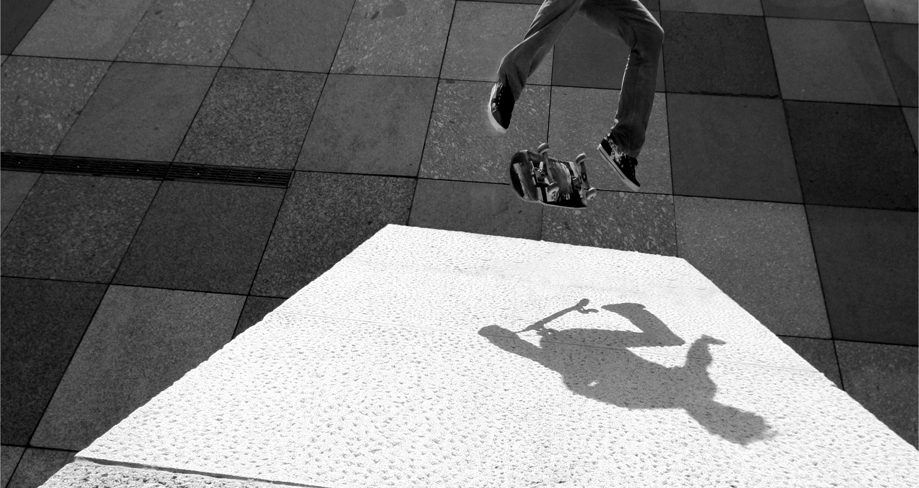 A skateboarder doing a kickflip on a slanted wall with their shadow showing