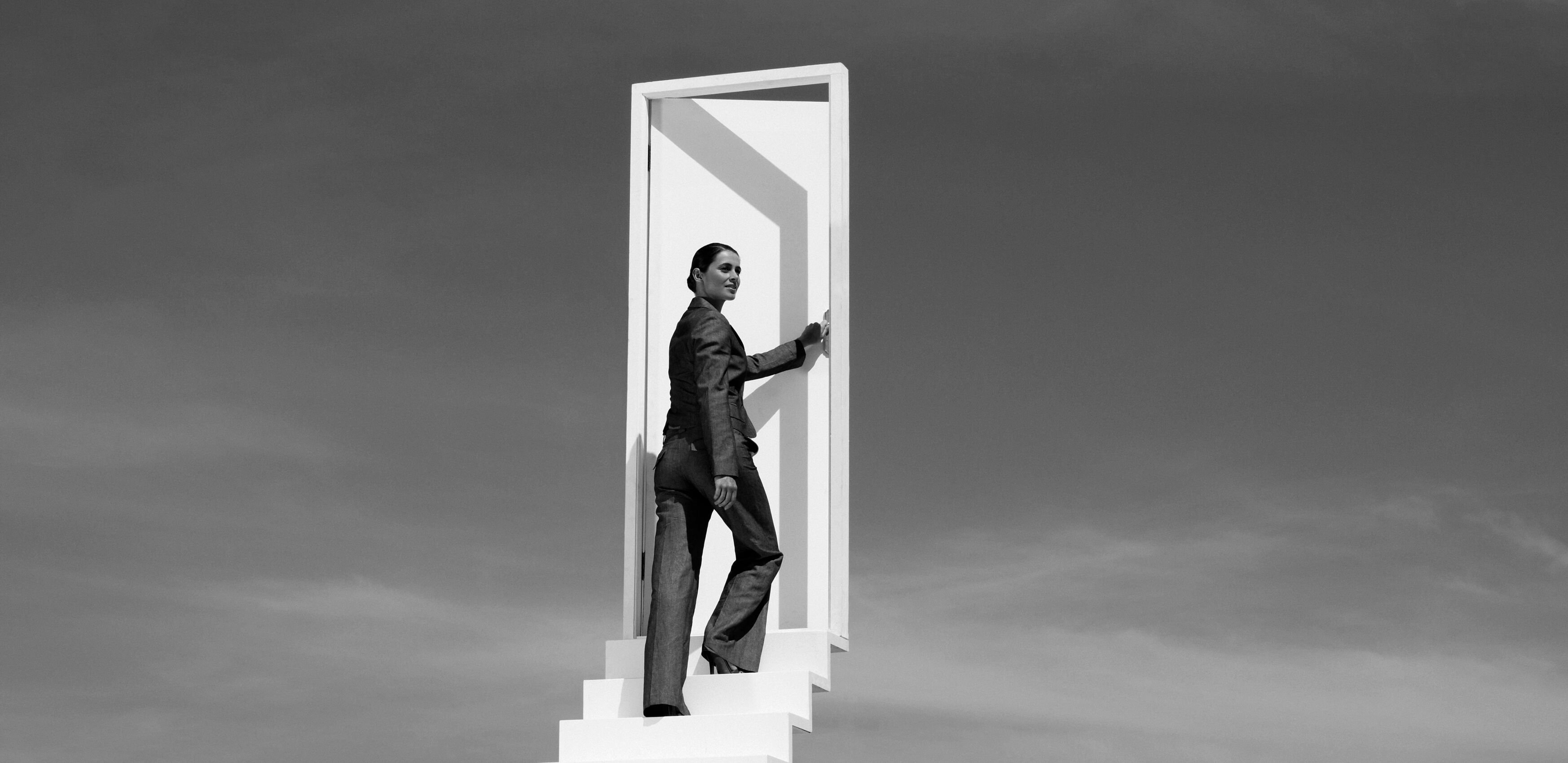 A woman walking up a set of stairs in the clouds, into and through a door