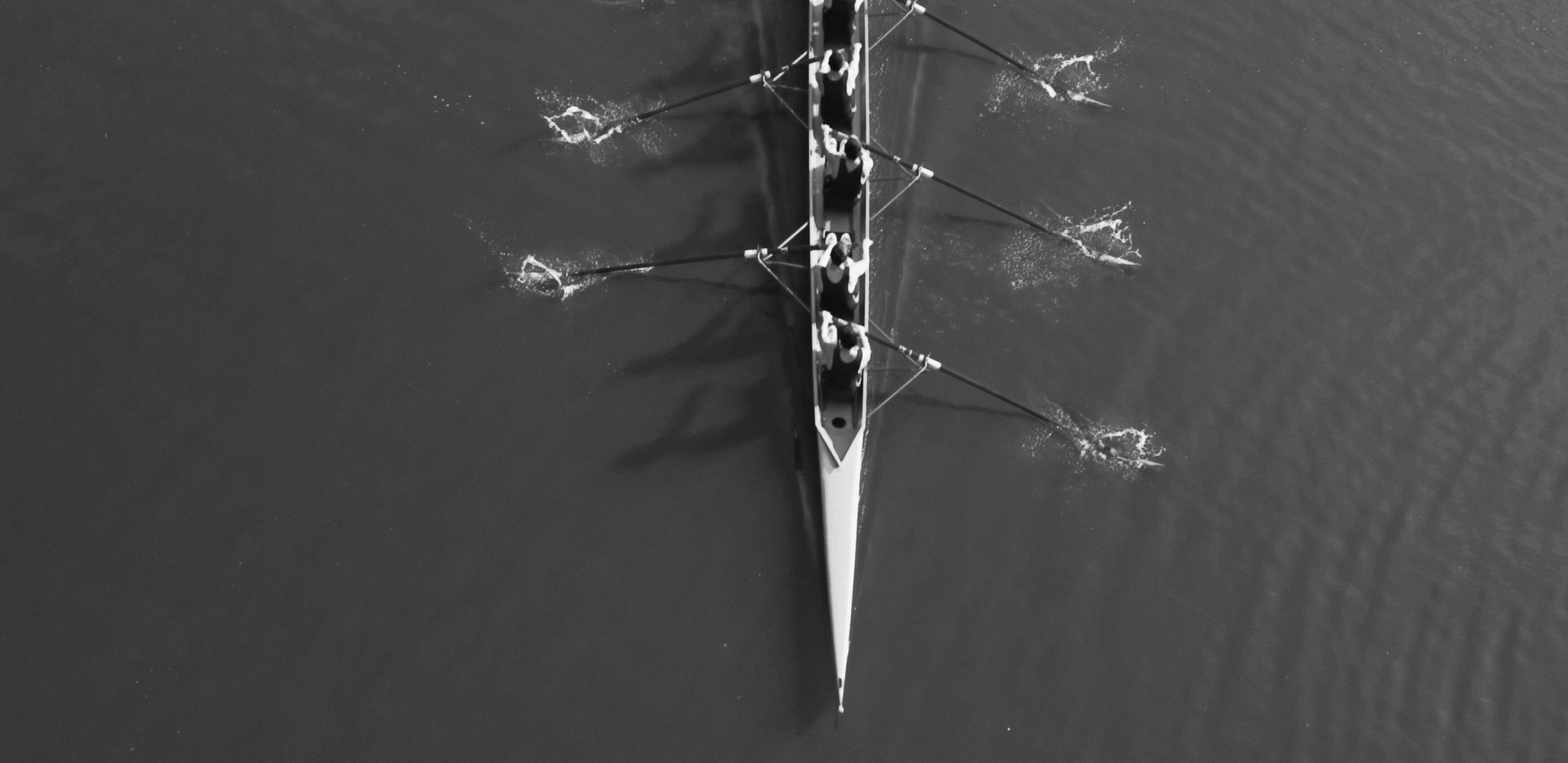 An image of a rowing boat, from above, with multiple men rowing on the water