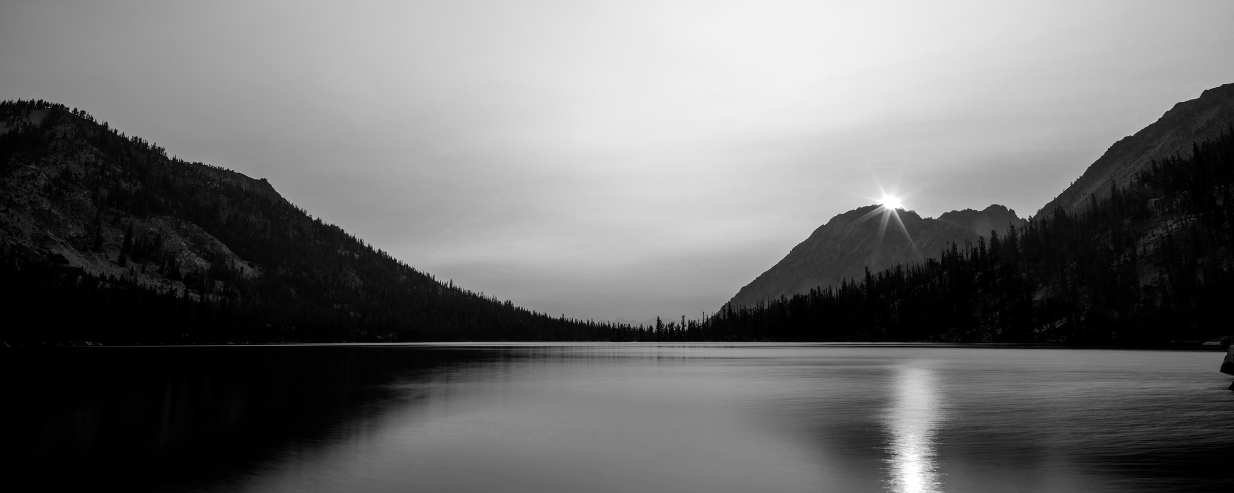 Sun shining over a peaceful lake surrounded by mountains