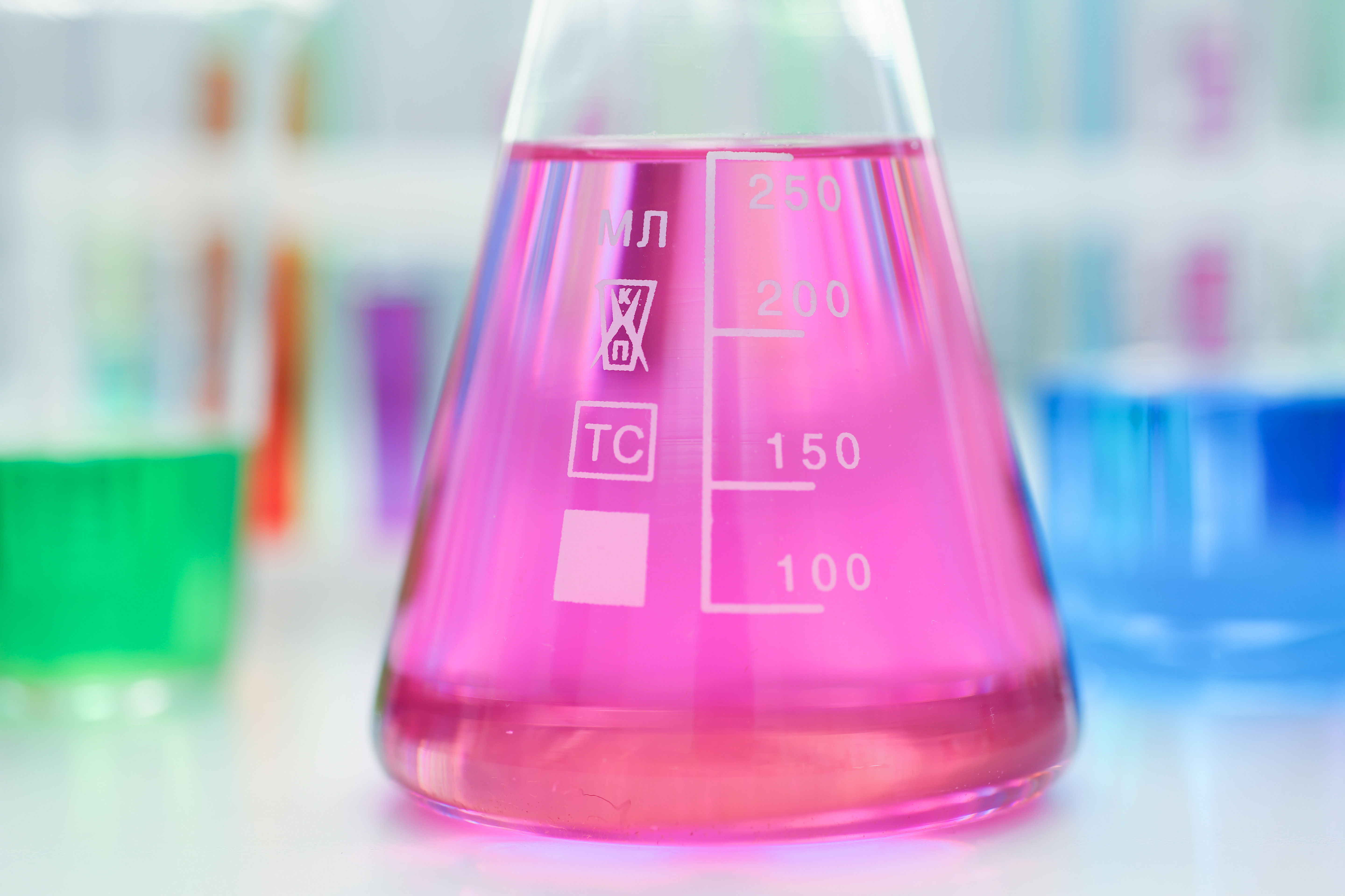 A laboratory experiment is shown with a pink liquid in a beaker amongst other beakers and glassware.