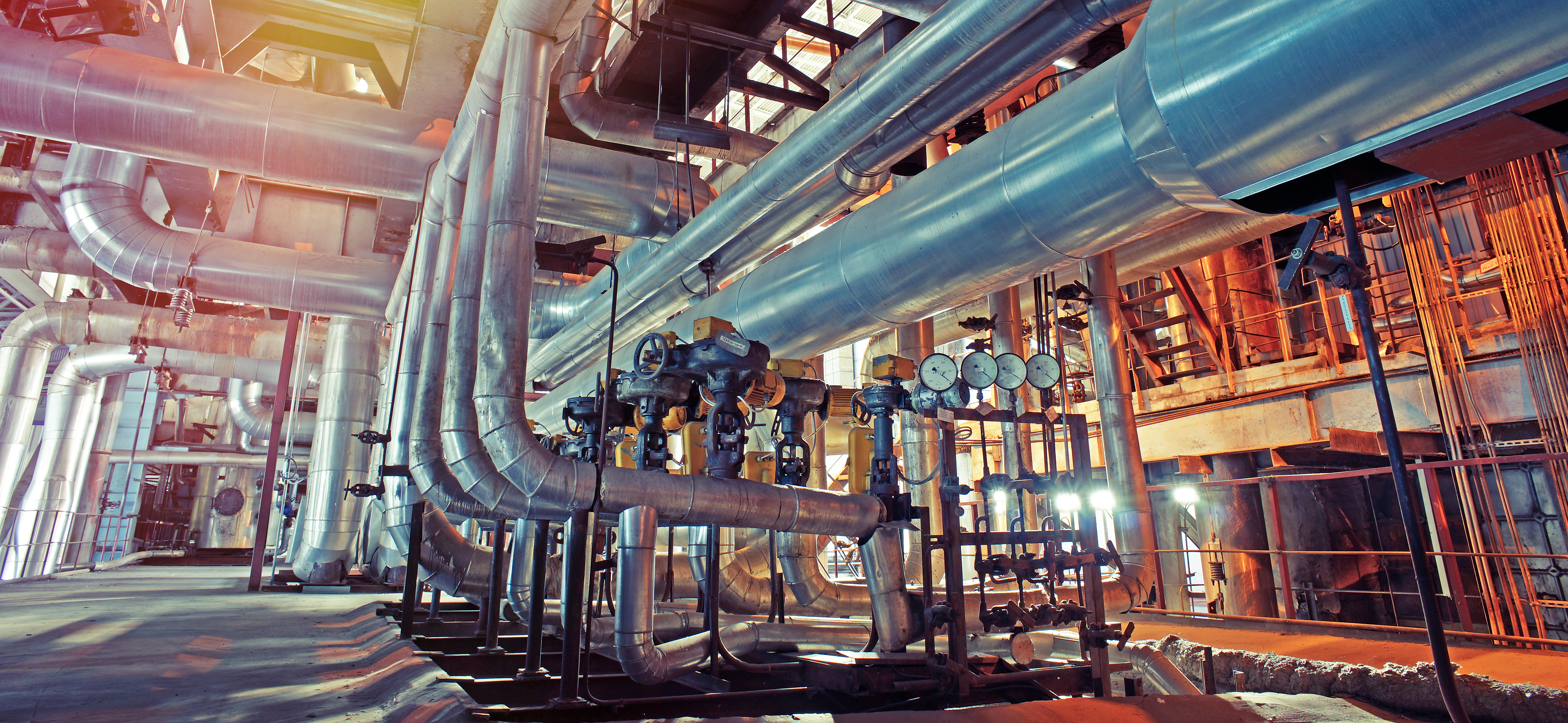 A complex network of pipes and valves are connected to several gauges and a large industrial furnace.