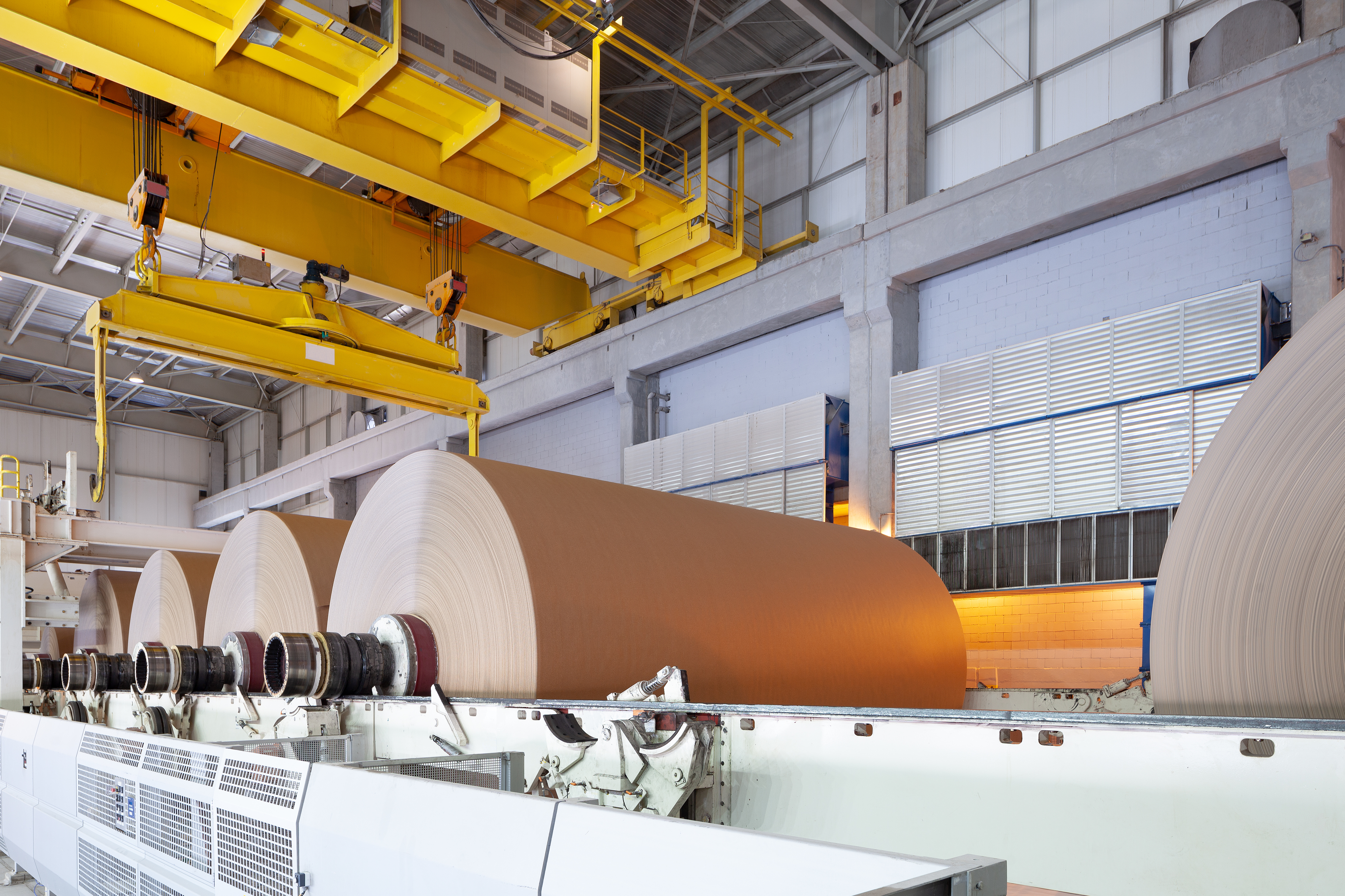 A large industrial facility produces large rolls of paper on a specialized piece of machinery.