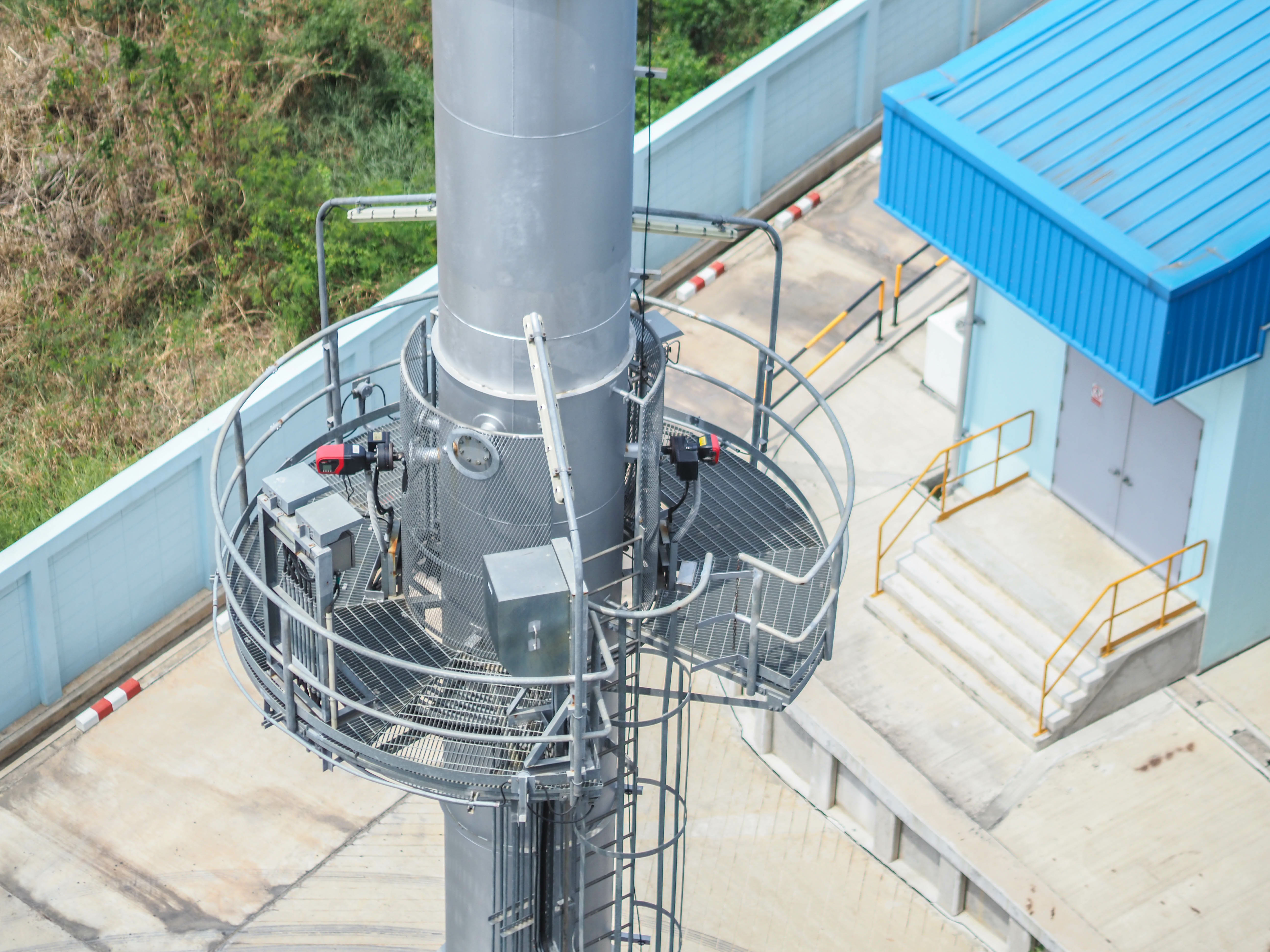 A metal staircase and platform surrounding a large metal pipe leads to a door on a building.