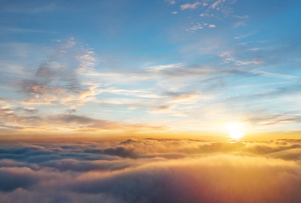The image shows a sunrise illuminating fluffy clouds in a clear blue sky.