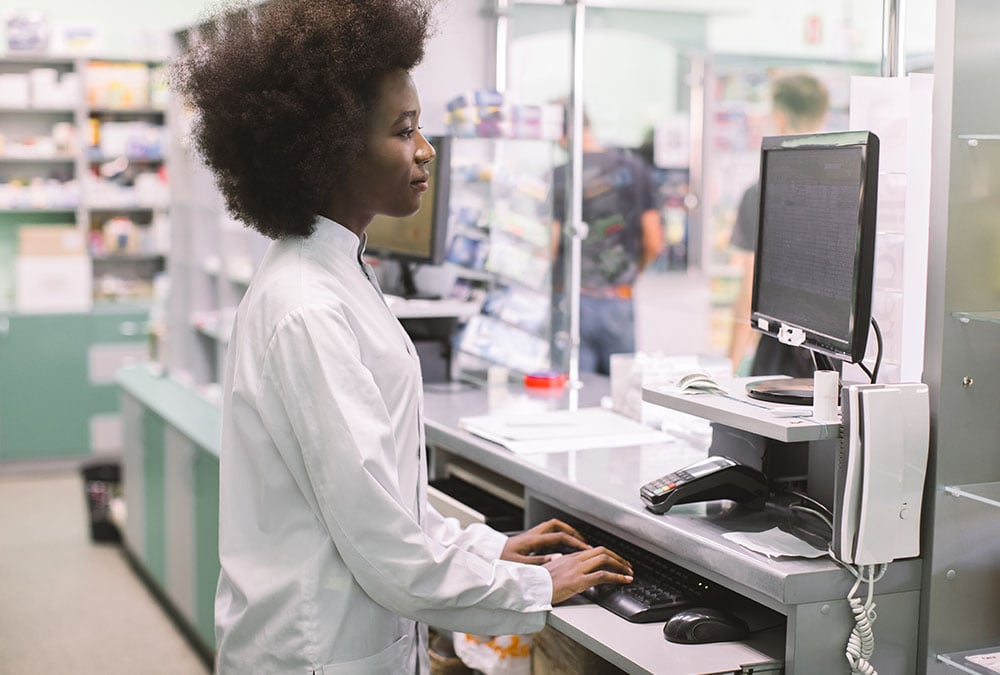 A pharmacist uses a computer to complete a transaction at the counter of a pharmacy.