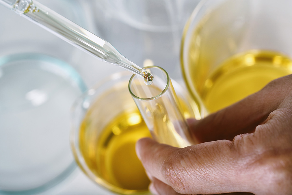 A scientist is carefully dropping liquid from a dropper into a test tube.