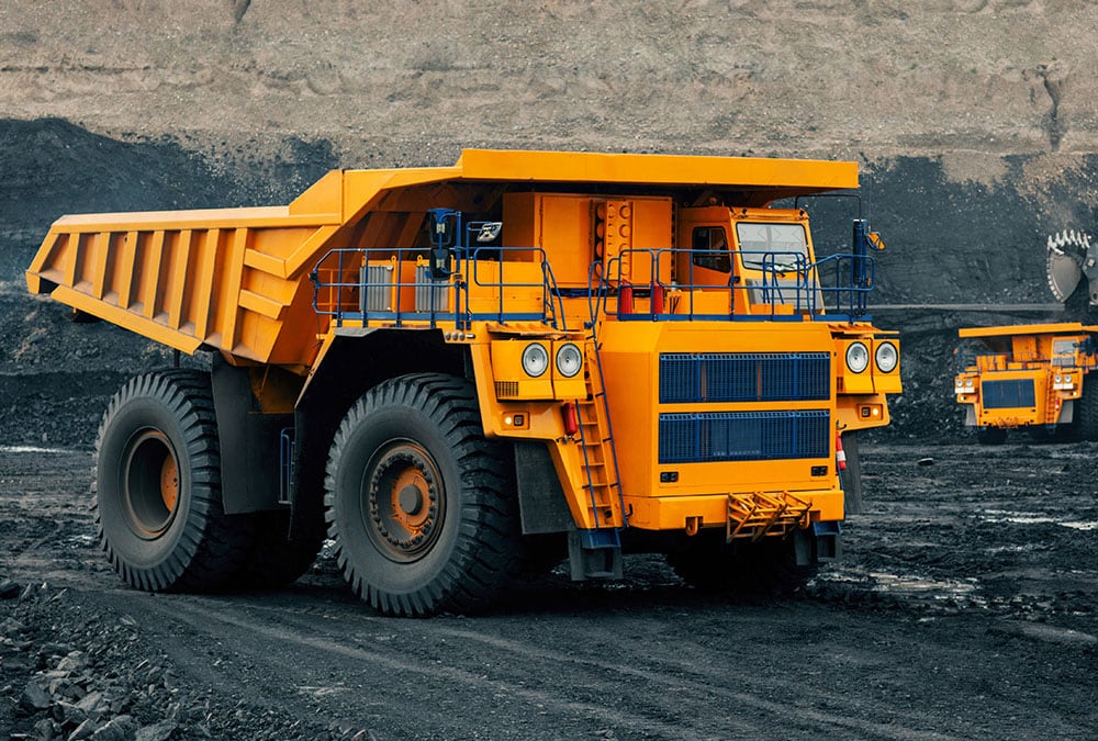 A large yellow dump truck is parked at a mine, likely used for hauling dirt or other materials.