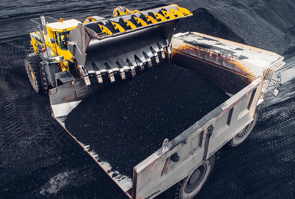 A large loader is dumping a load of black gravel into a dump truck.