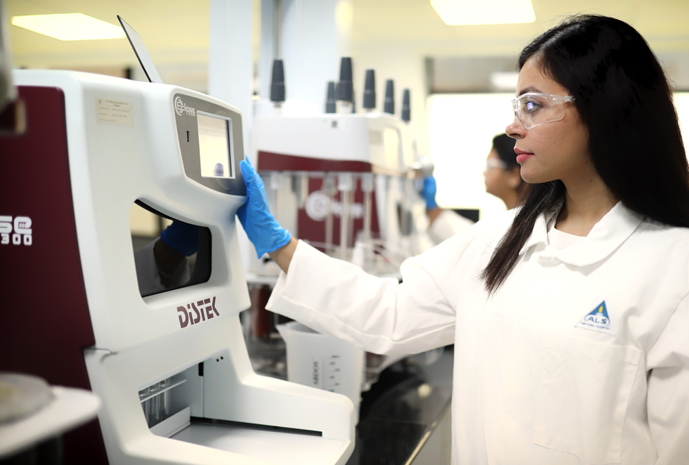 A female scientist in a lab coat operates a testing device.