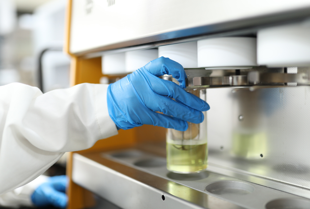 A scientist in a lab coat uses a gloved hand to insert a sample into a testing machine.