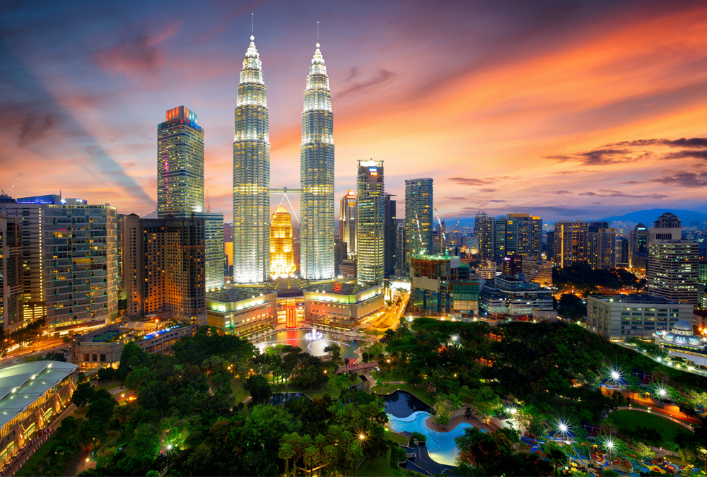The Kuala Lumpur skyline at dusk, with the Petronas Towers prominently featured in the foreground.