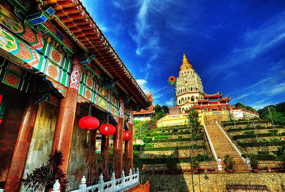 A colorful temple sits on a hill overlooking a lush, green valley.