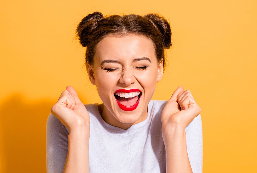 A smiling woman with her hands in the air excitedly celebrates.