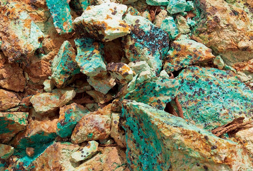 The image shows a collection of rocks covered in green copper ore, likely collected as part of an exploratory or mining operation.