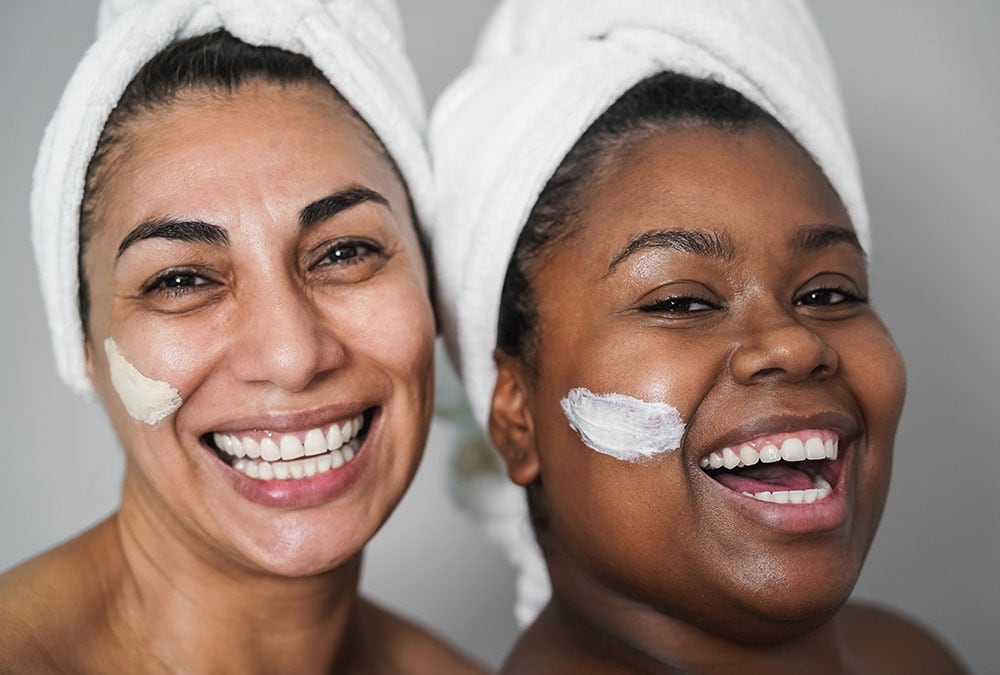 Two women have face masks applied and smile for the camera.