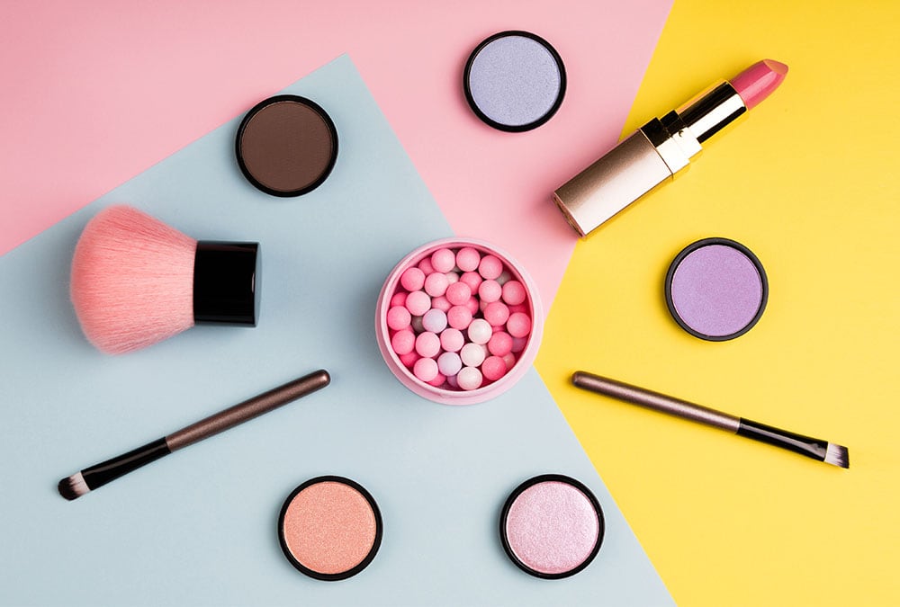 The image shows makeup products, including brushes, lipstick, eyeshadow, and powder.