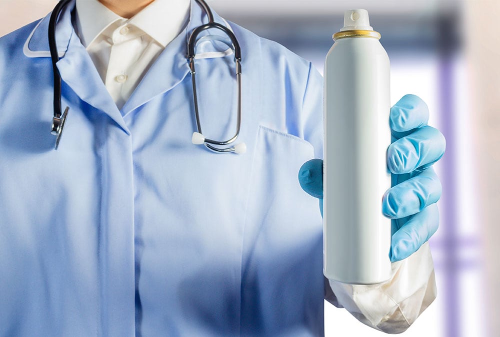 A doctor wearing blue gloves is holding an aerosol can that may be an inhaler.