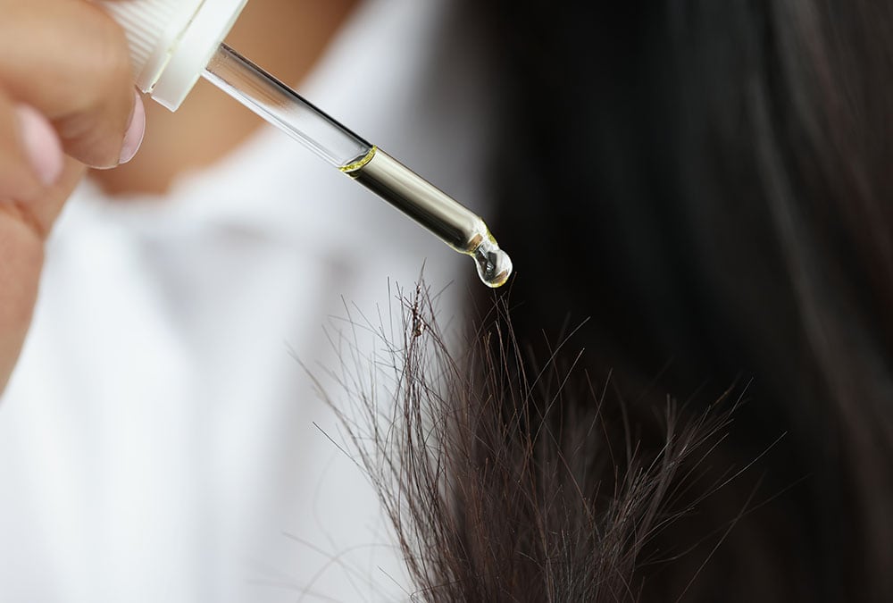 A woman applies oil to her hair.
