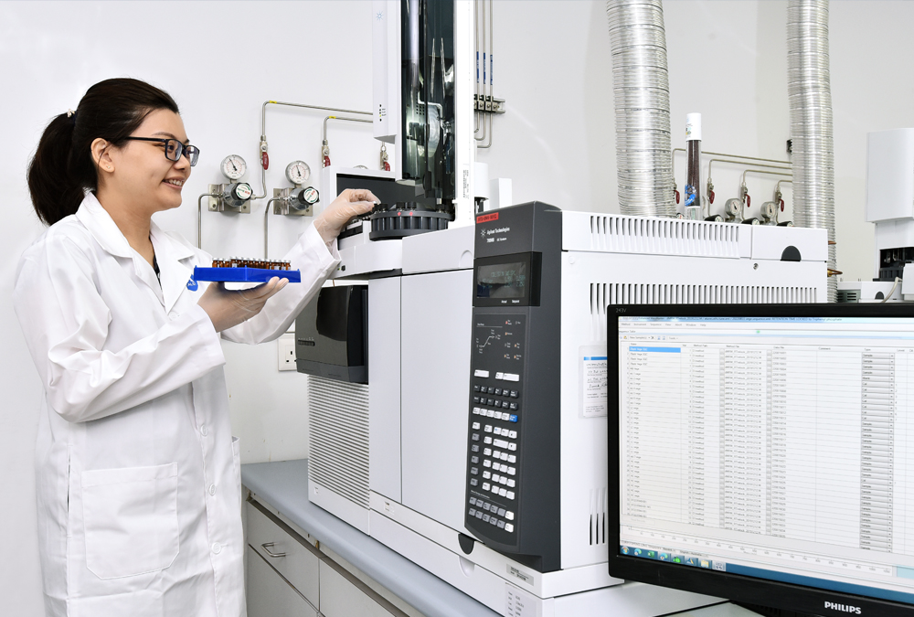 A woman in a lab coat performs an experiment to test a sample in a scientific analysis lab, using specialized equipment.