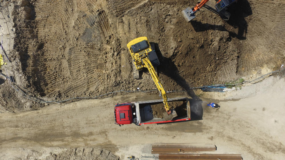A yellow excavator is dumping dirt into a red dump truck on a construction site.