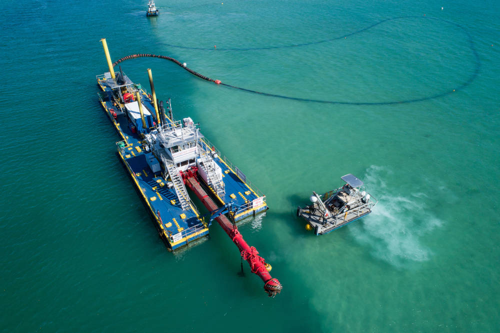 A large dredge boat is anchored with a smaller support boat nearby.